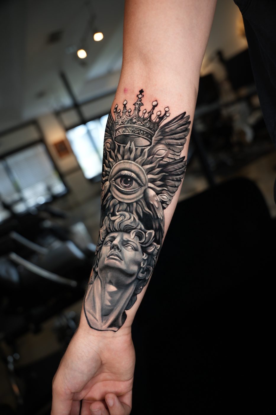 Estatua clásica con ojo, alas y corona en el antebrazo